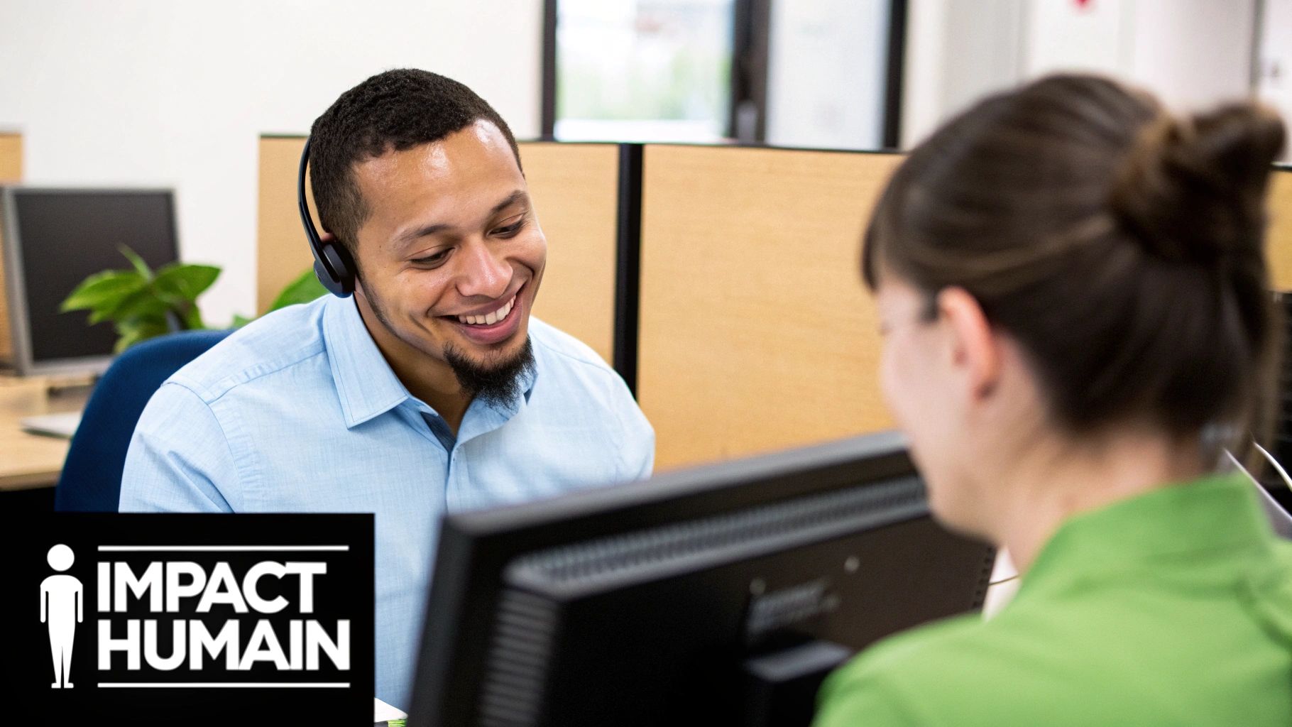 Homme souriant avec un casque, interagissant avec une collègue dans un environnement de bureau moderne.