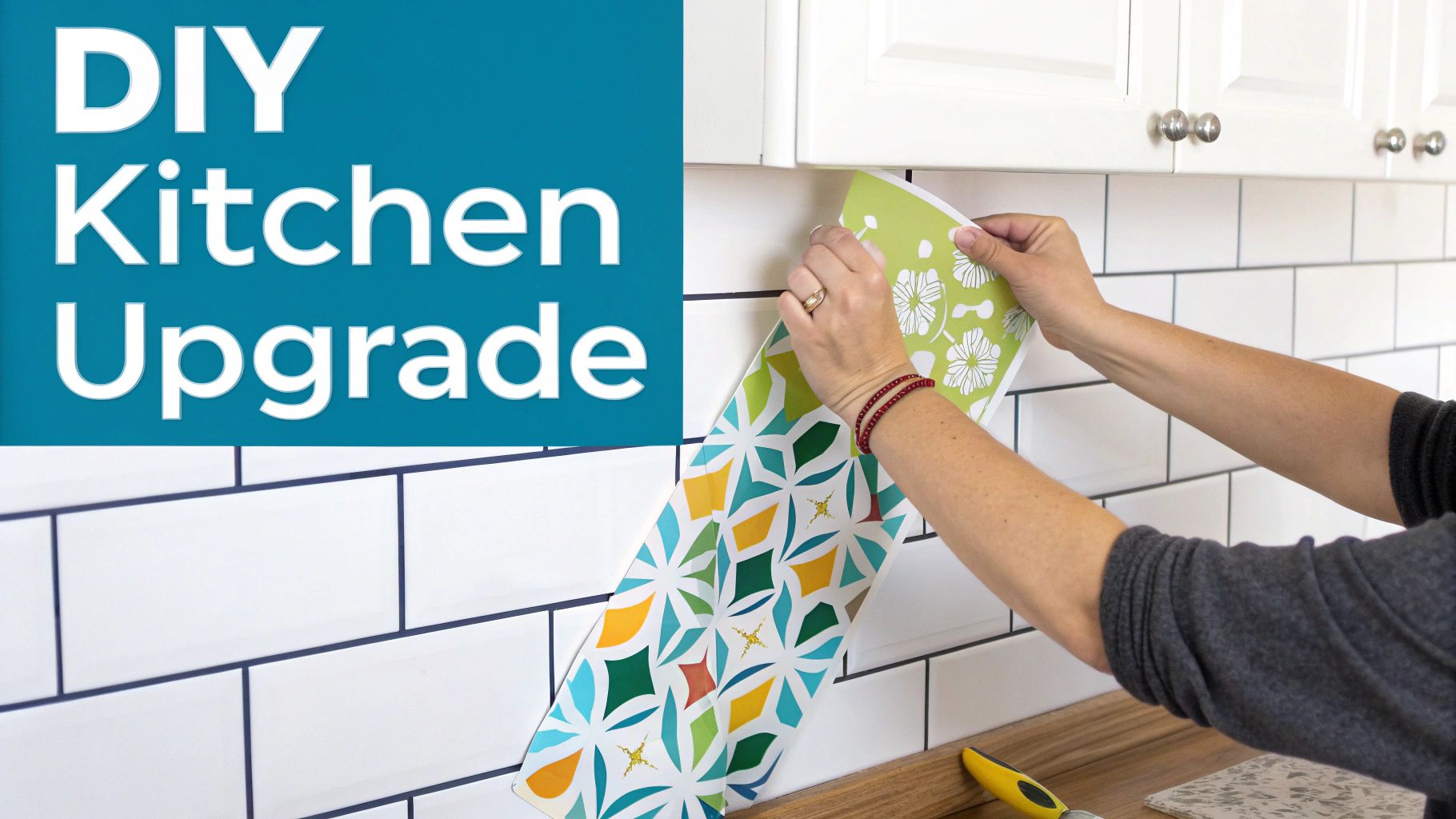 Hands applying colorful patterned stickers to a white subway tile kitchen backsplash under white cabinets.