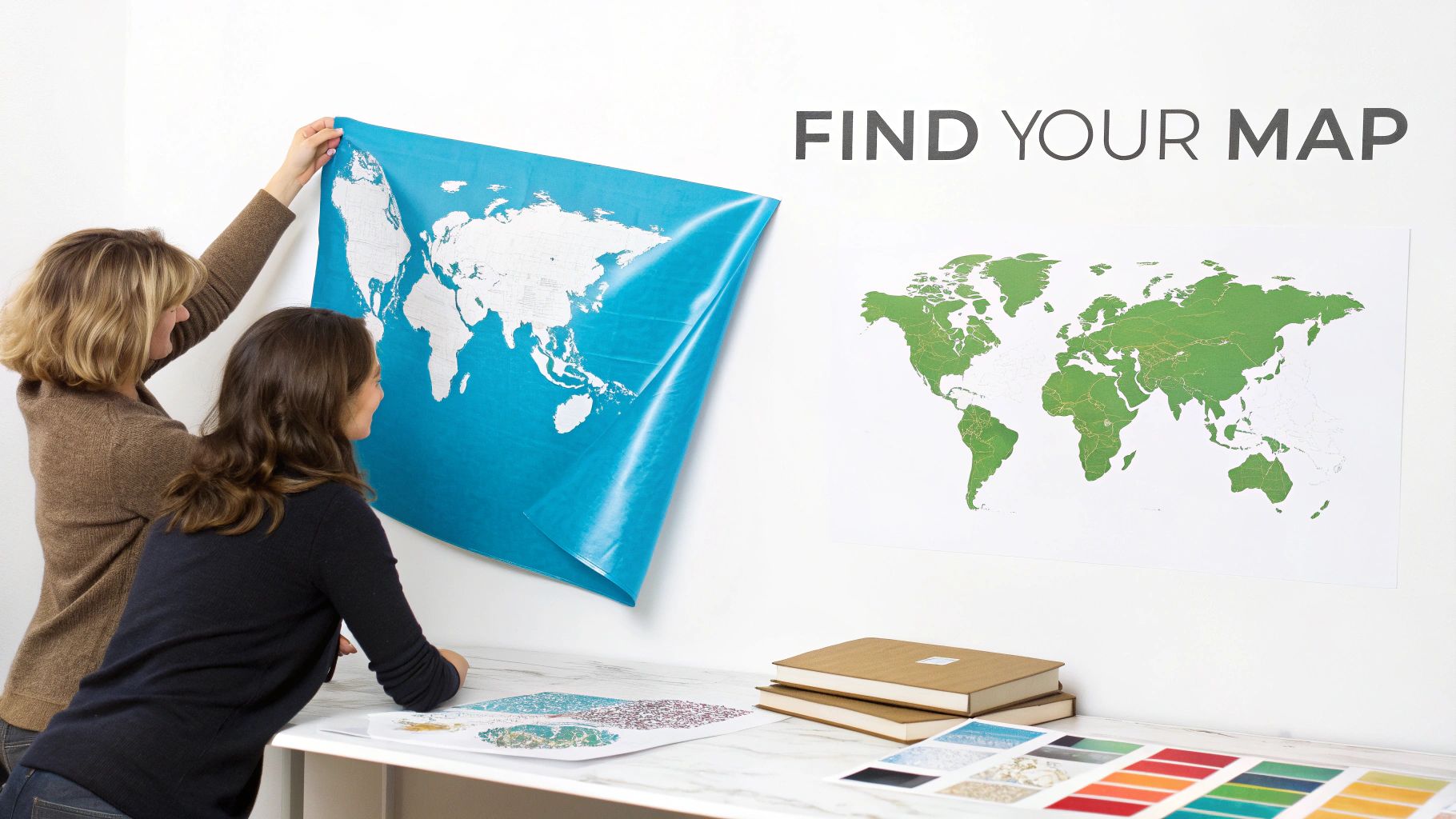 Two women apply a blue world map wall decal, with another map and design swatches on a table.