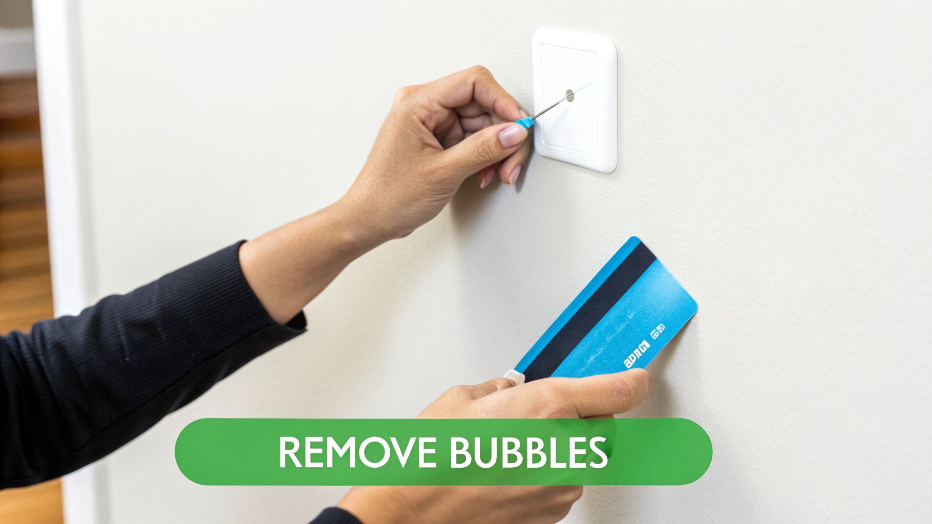 A person uses a small blue-tipped tool to prick a white device on a wall, with a blue card nearby.