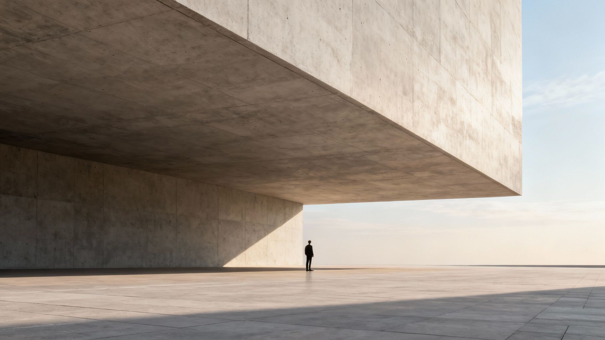 A lone figure stands under a vast, minimalist concrete structure with strong geometric shadows.