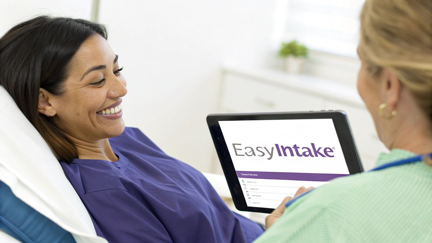 Smiling patient in a hospital gown looks at a digital intake form on a tablet held by a healthcare professional.