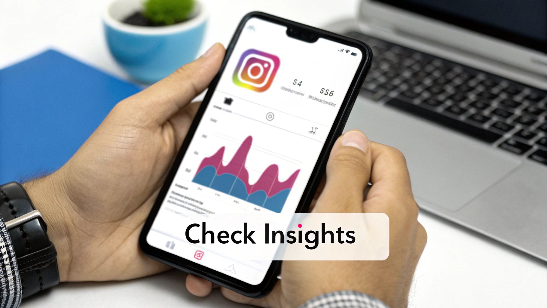 Close-up of hands holding a smartphone displaying Instagram analytics, charts, and data, with a laptop in the background.