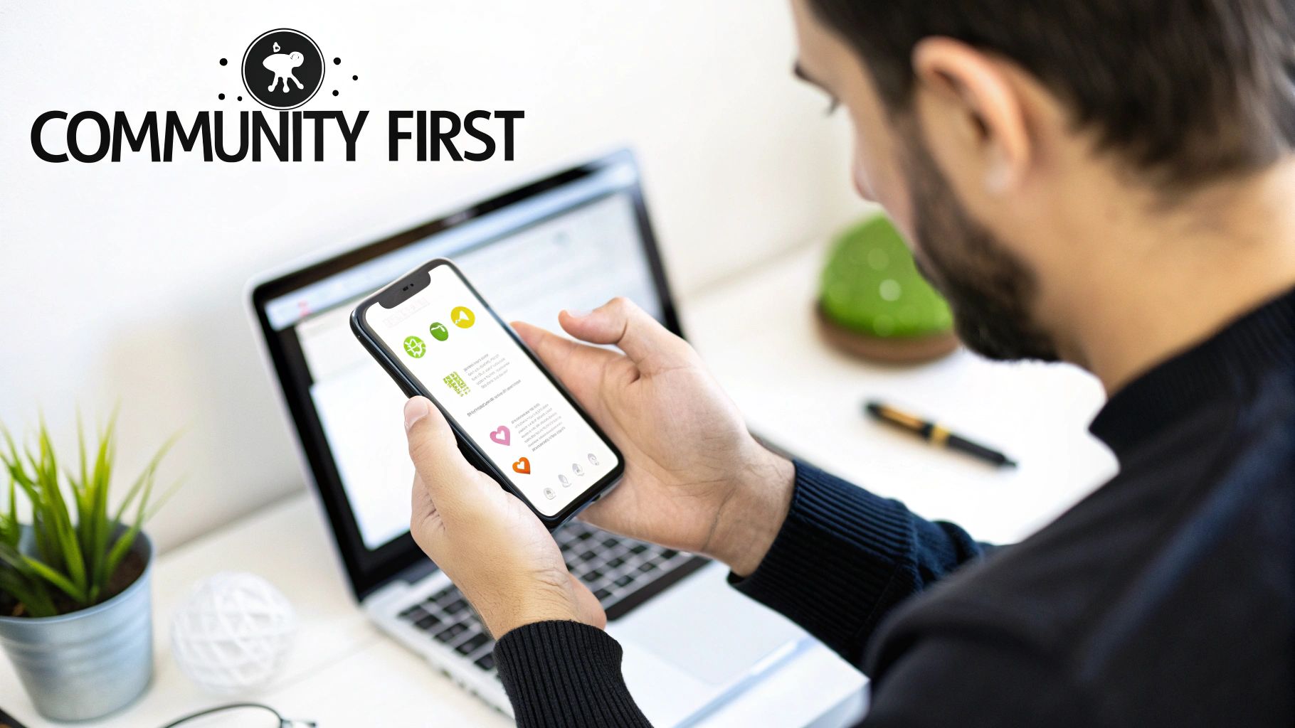 A person holding a smartphone showing an app with green icons, working on a laptop.