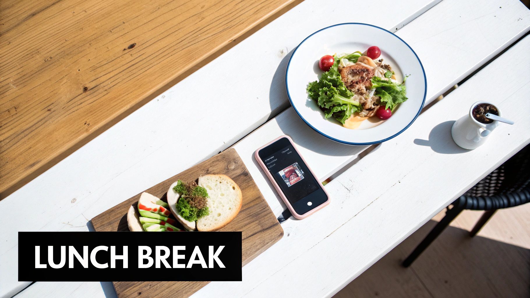 Overhead view of a salad, sandwich, smartphone, and drink on an outdoor table during lunch.