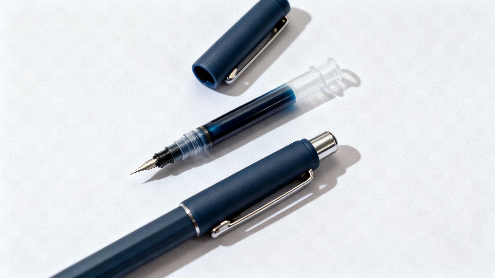 A disassembled dark blue fountain pen with its clear ink converter filled with blue ink on white.