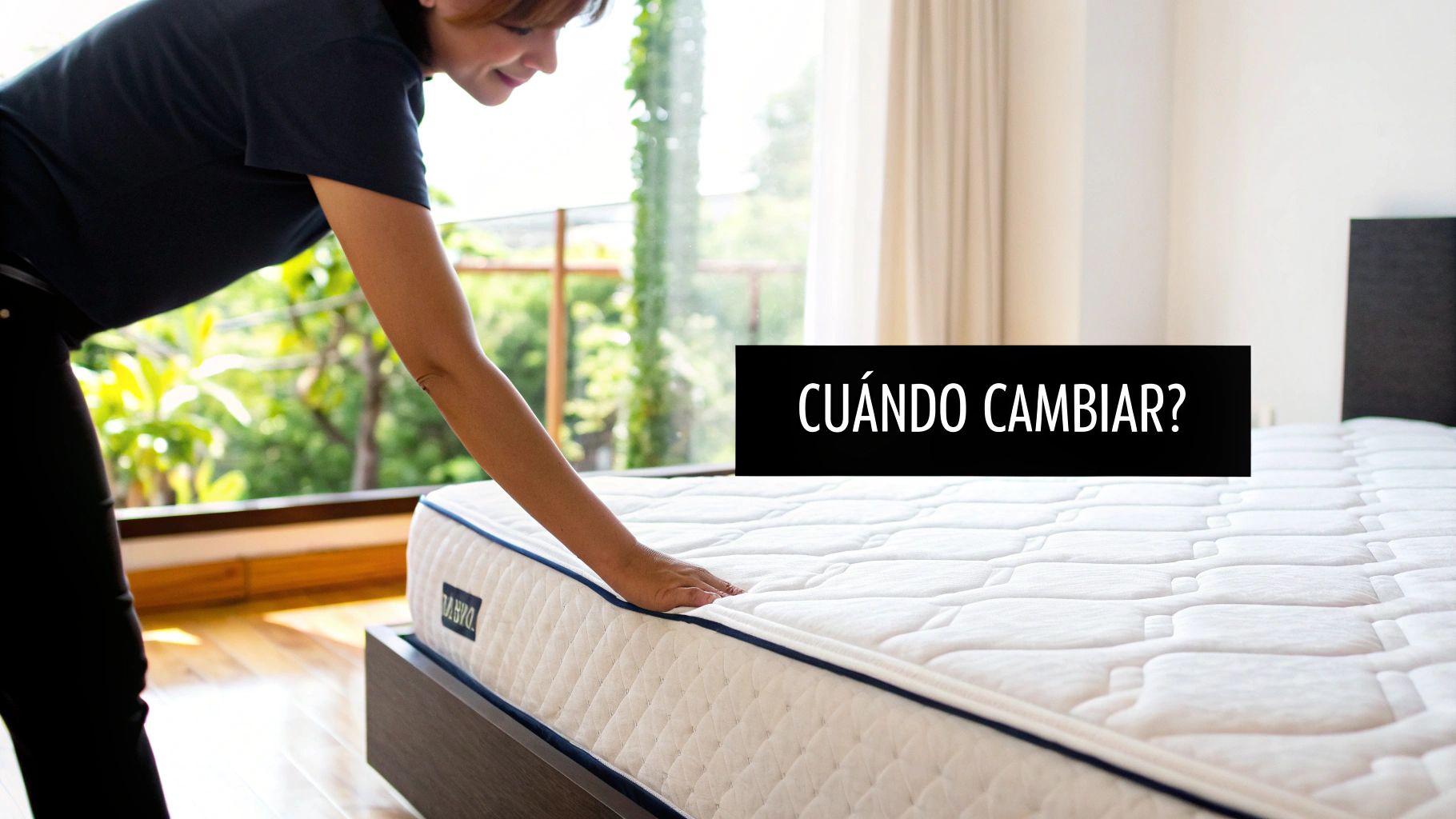 Mujer tocando un colchón blanco y acolchado en un dormitorio luminoso con vistas a la naturaleza.
