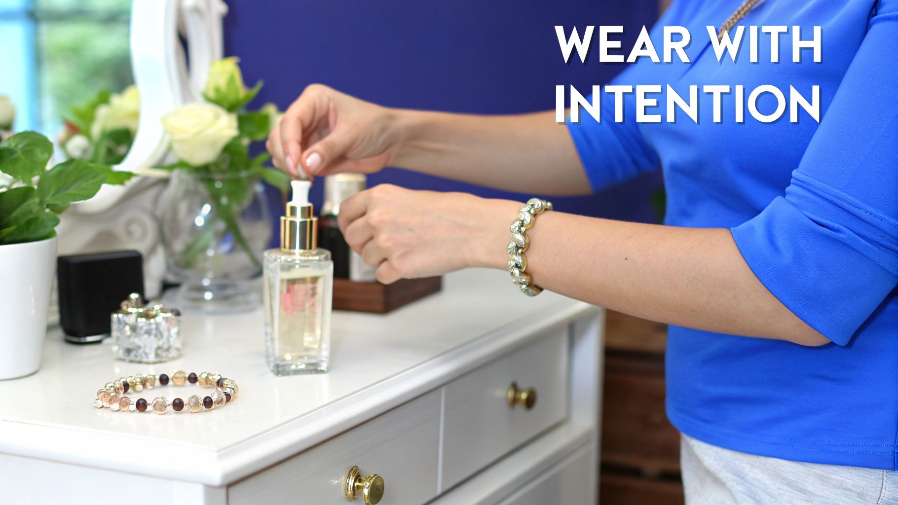 A woman in a blue top applies perfume from a bottle on a white dresser with jewelry.