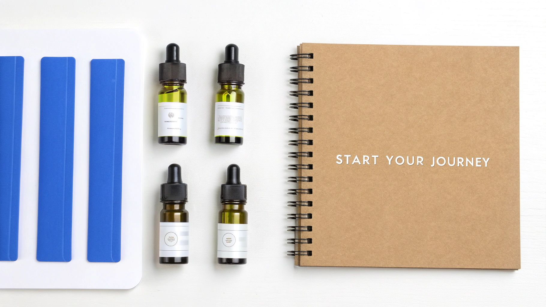 Four dropper bottles with green liquid and a brown notebook titled 'START YOUR JOURNEY' on a white surface.
