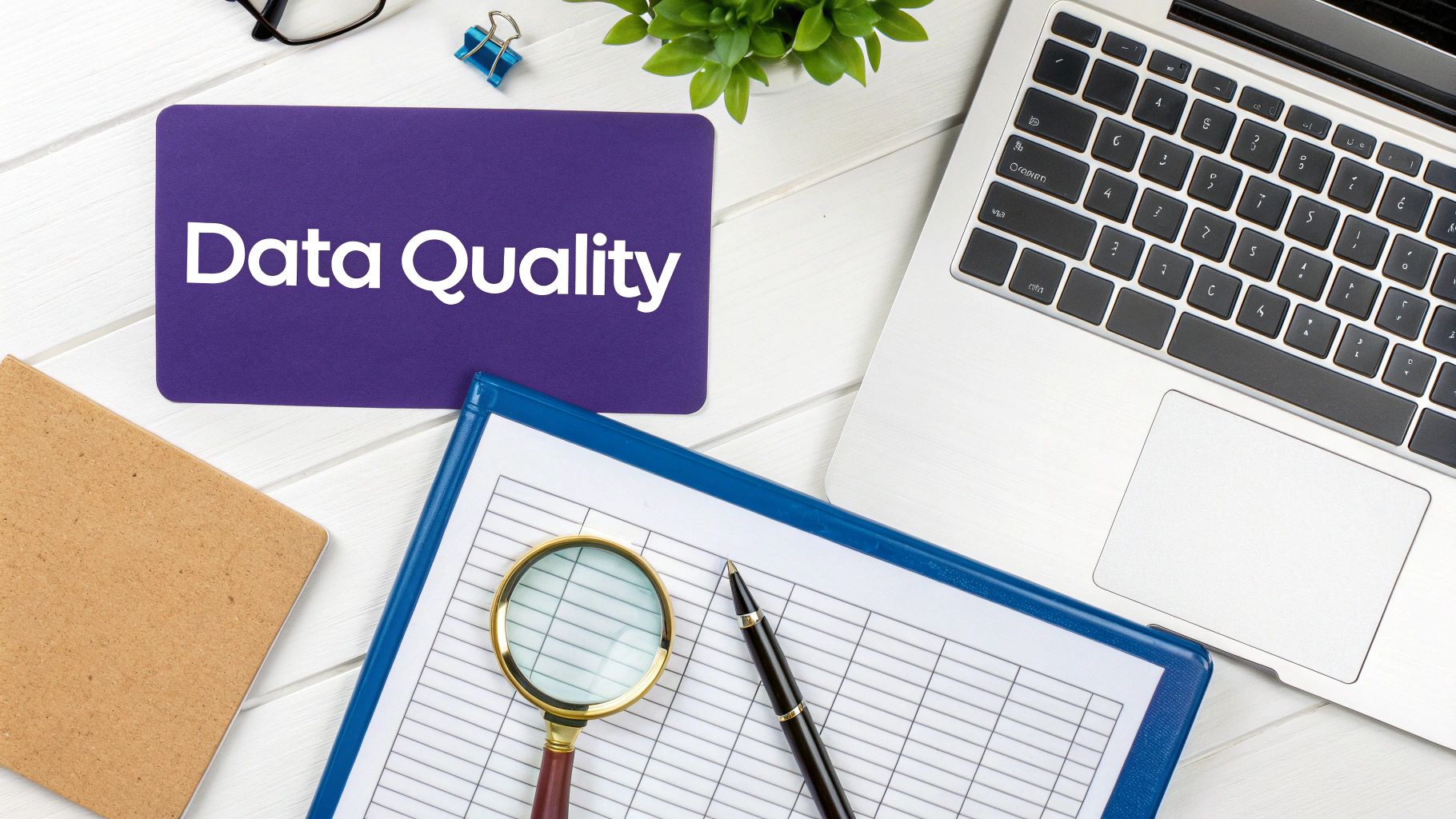 Overhead view of a desk with a 'Data Quality' sign, laptop, magnifying glass, and documents.