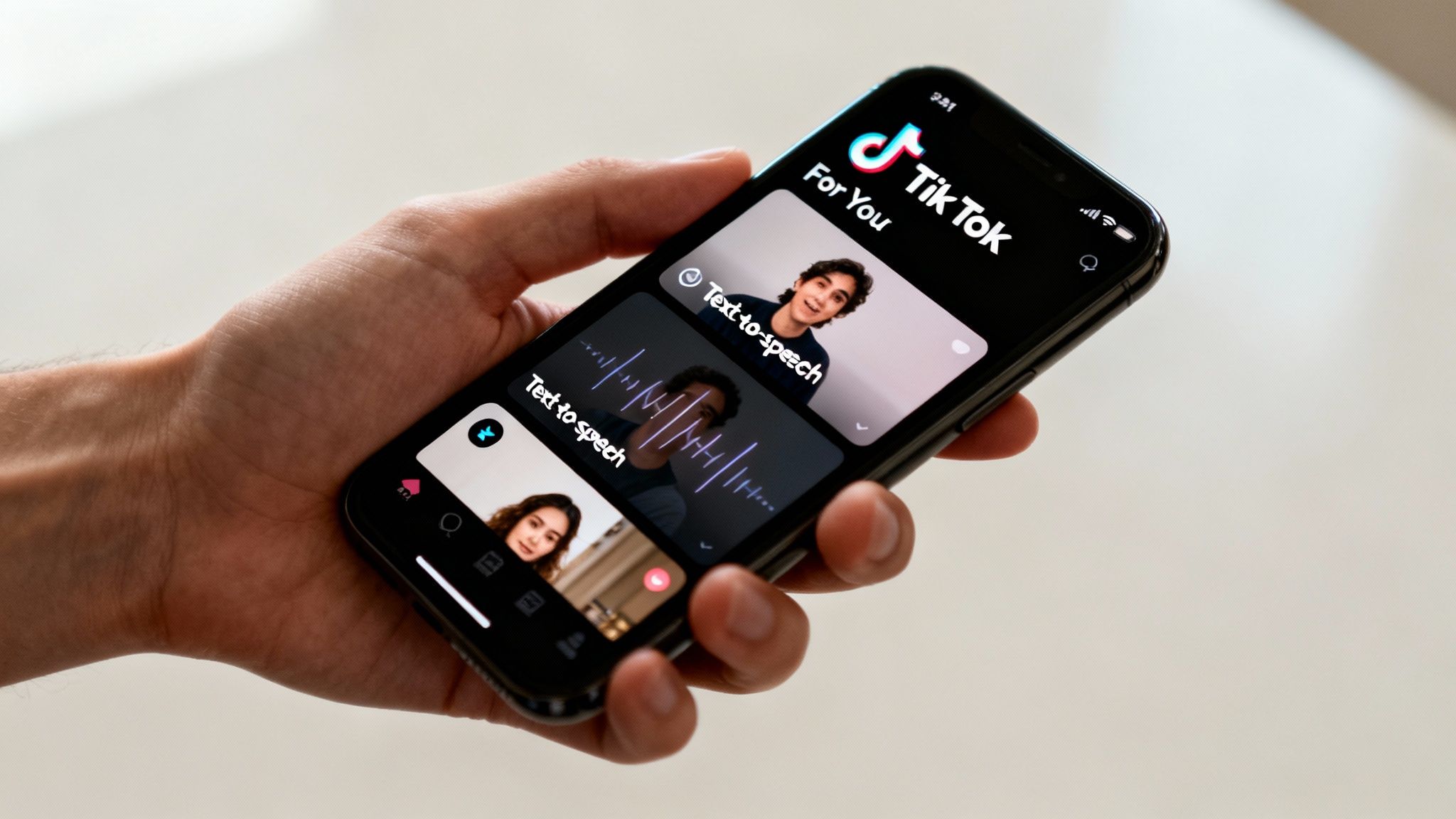 A hand holds an iPhone displaying the TikTok app with two text-to-speech videos on the screen.