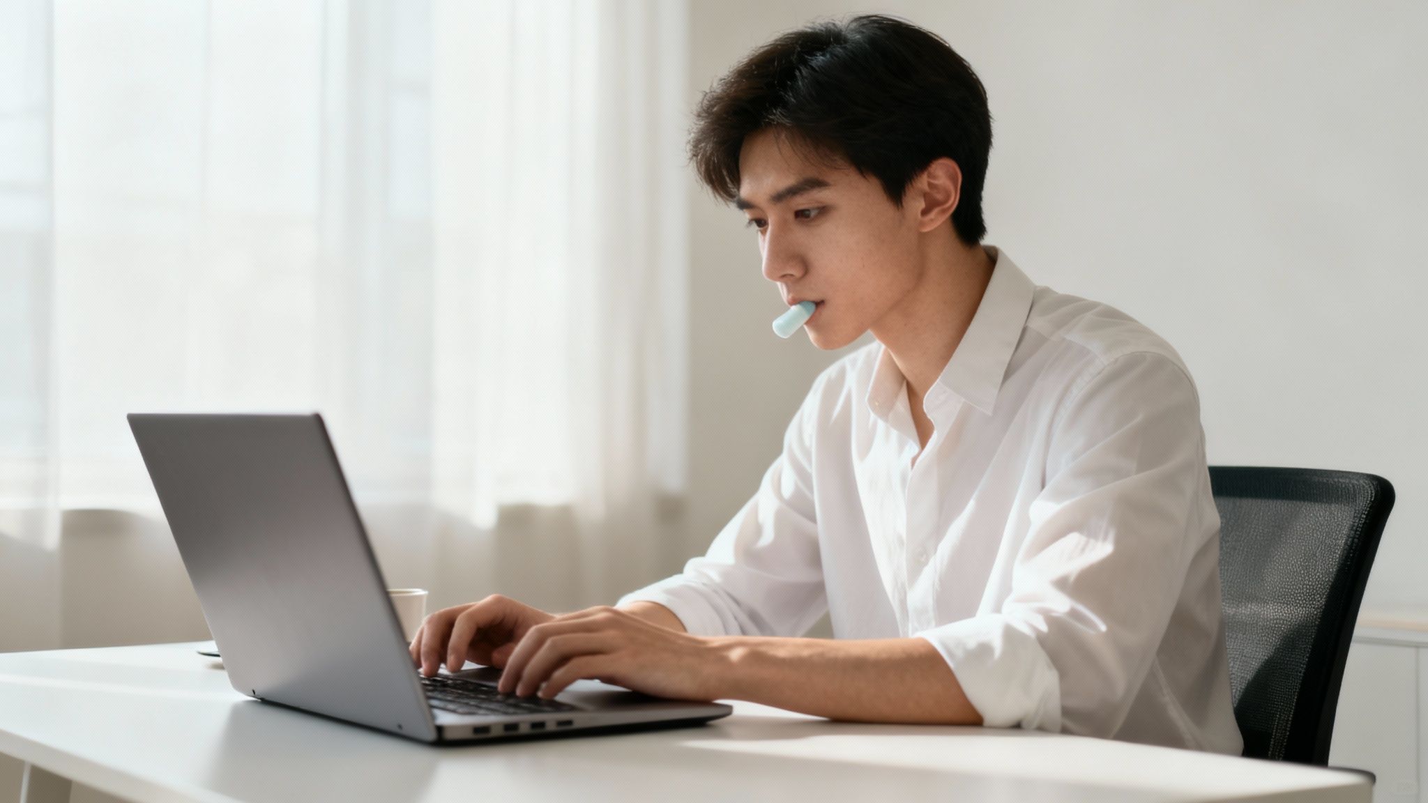 A person chewing gum while working on a laptop, looking focused and calm.