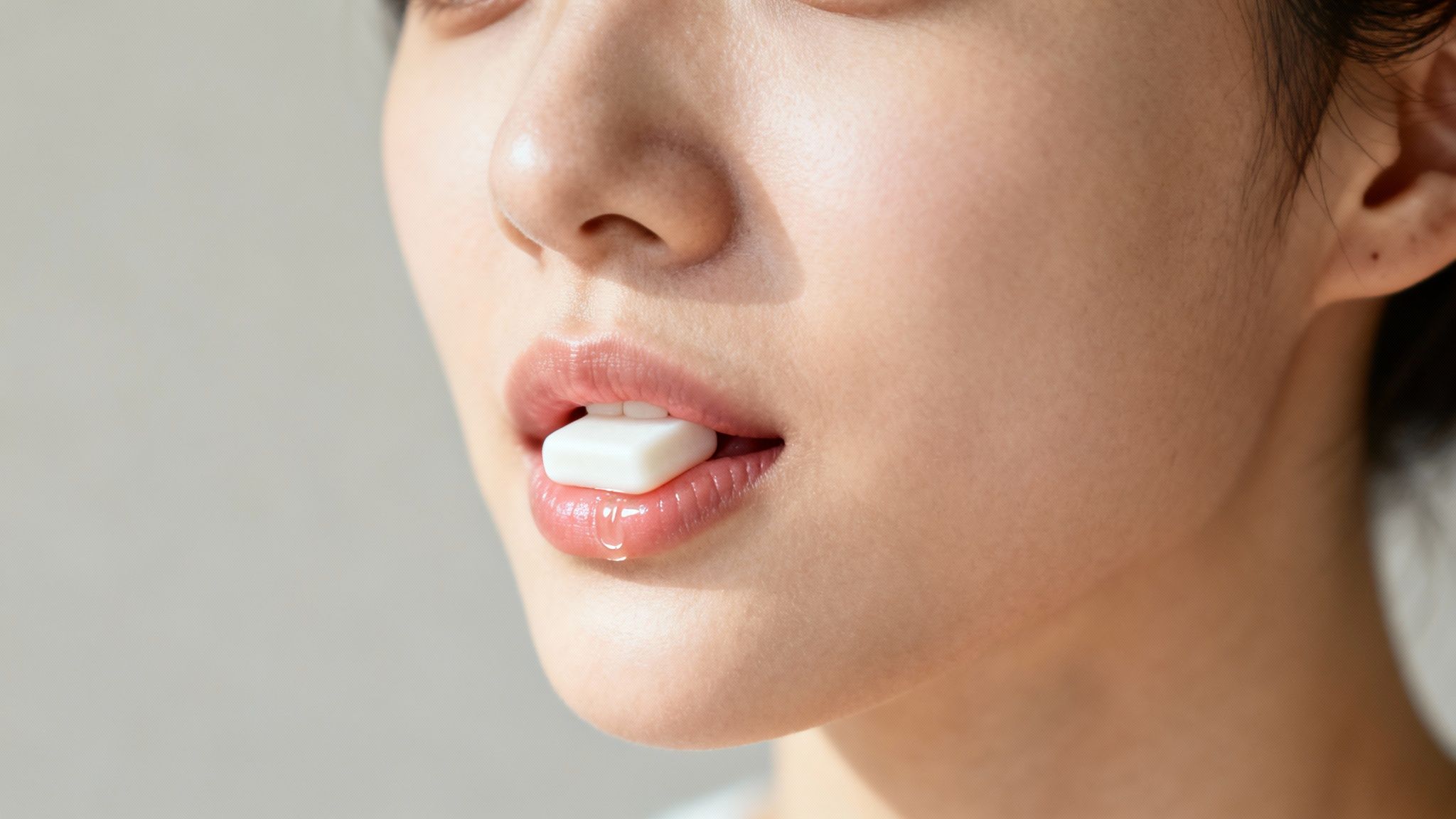 Close-up of a person's mouth with a white chewing gum piece held between glossy lips.