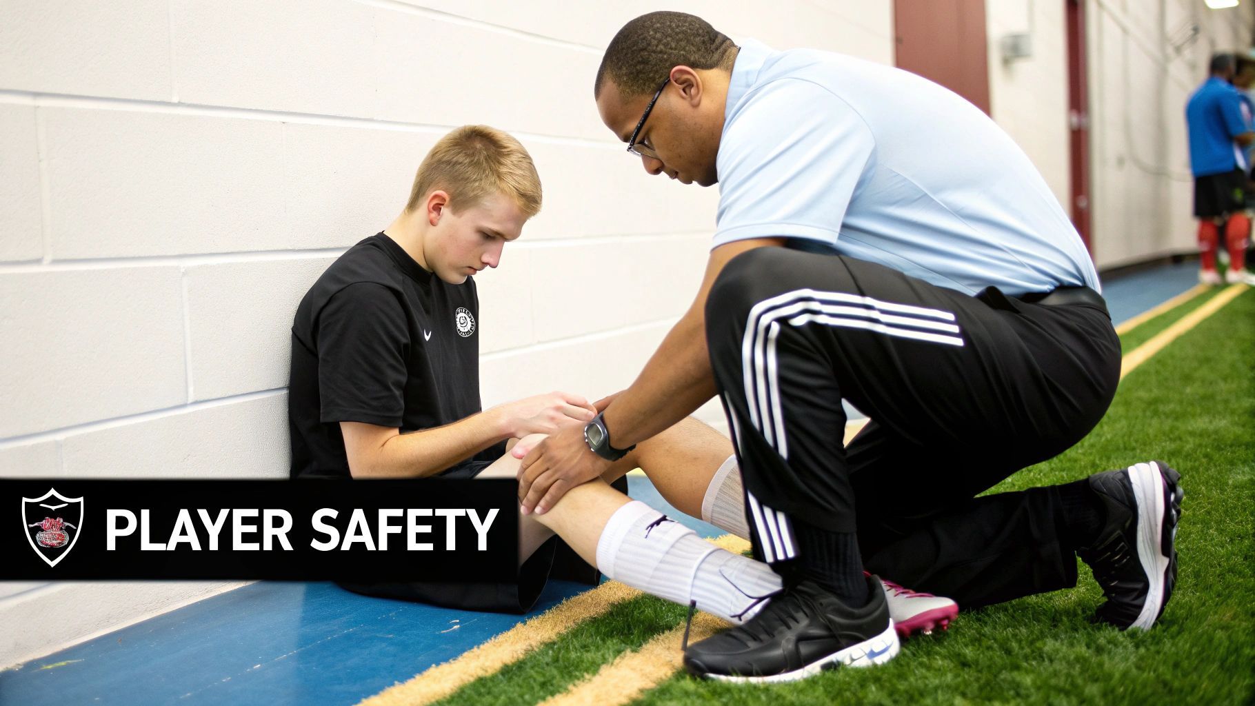 An athletic trainer kneels to examine a young male soccer player's leg injury on an indoor turf field, emphasizing player safety.