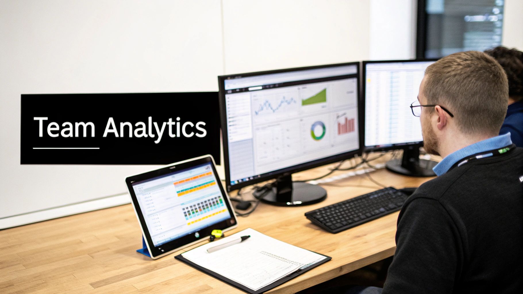A person reviews 'Team Analytics' data on multiple computer monitors and a tablet.