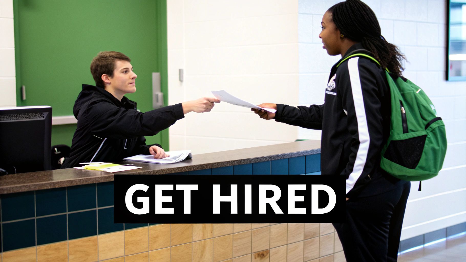Student receiving employment documents at athletic facility reception desk with green backpack