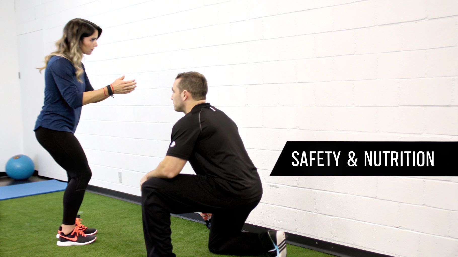 A woman in athletic wear performing an exercise while a man kneels nearby, providing instruction in a gym.