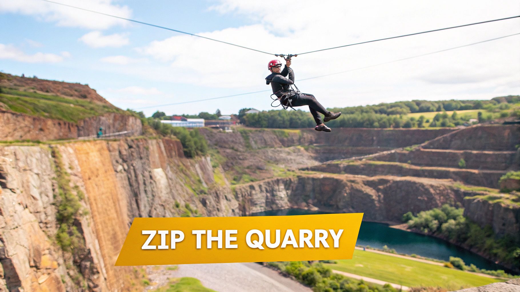 A person in a red helmet zip-lining across a vast quarry with steep cliffs and a blue lake.