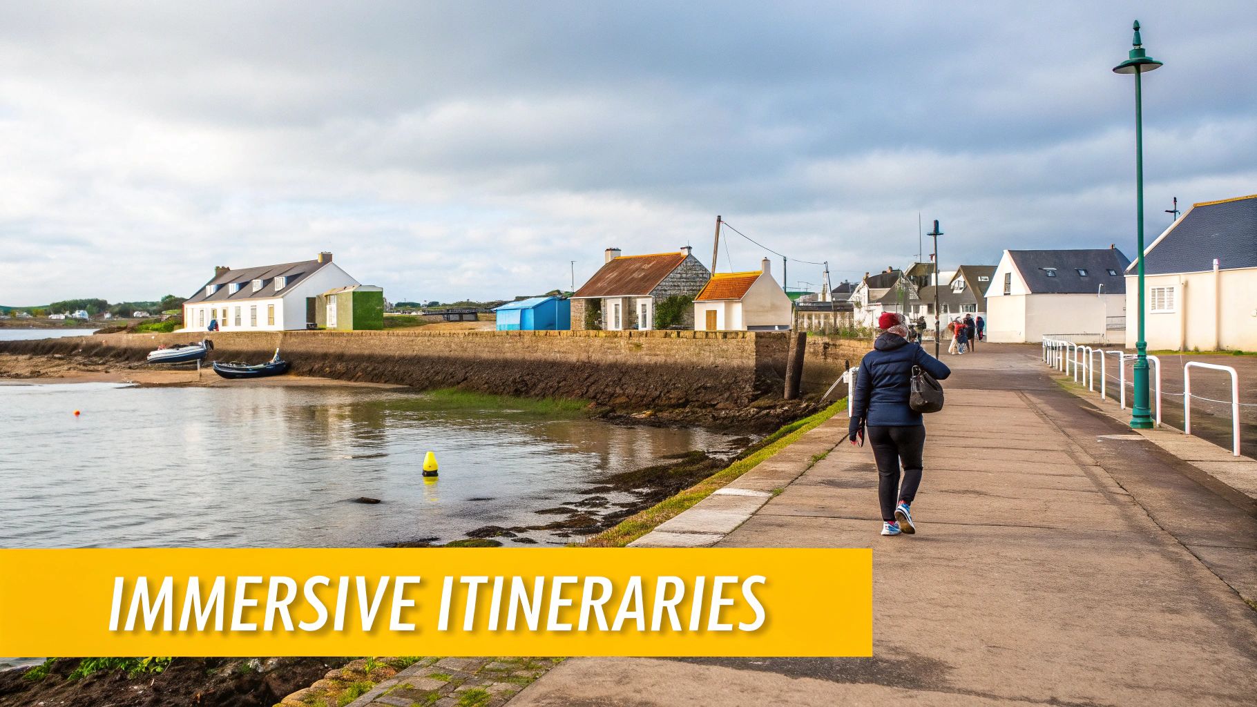 A person walks along a coastal promenade with colorful houses lining the water's edge and boats.