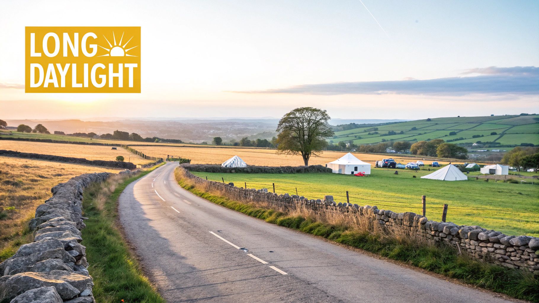A scenic winding road through green fields with stone walls, distant hills, and tents under a long daylight sky.