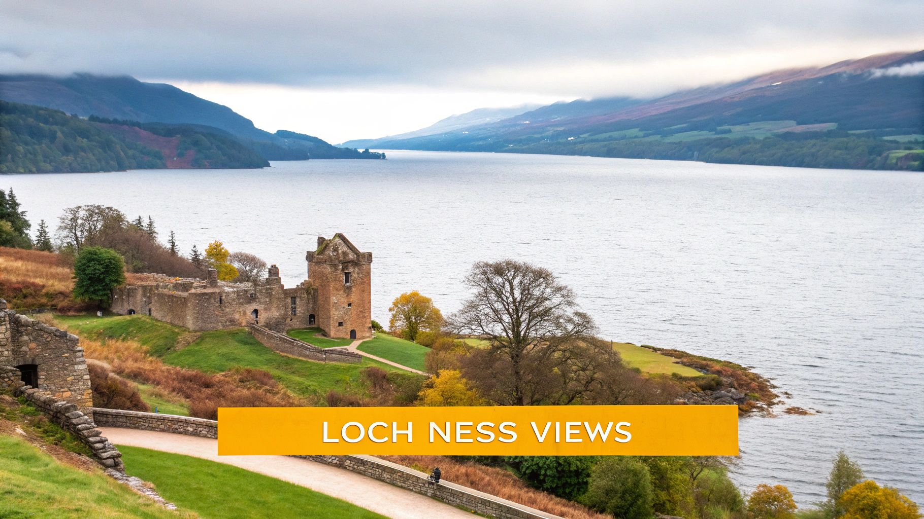 A wide view of Urquhart Castle ruins beside the vast Loch Ness with misty mountains in Scotland.