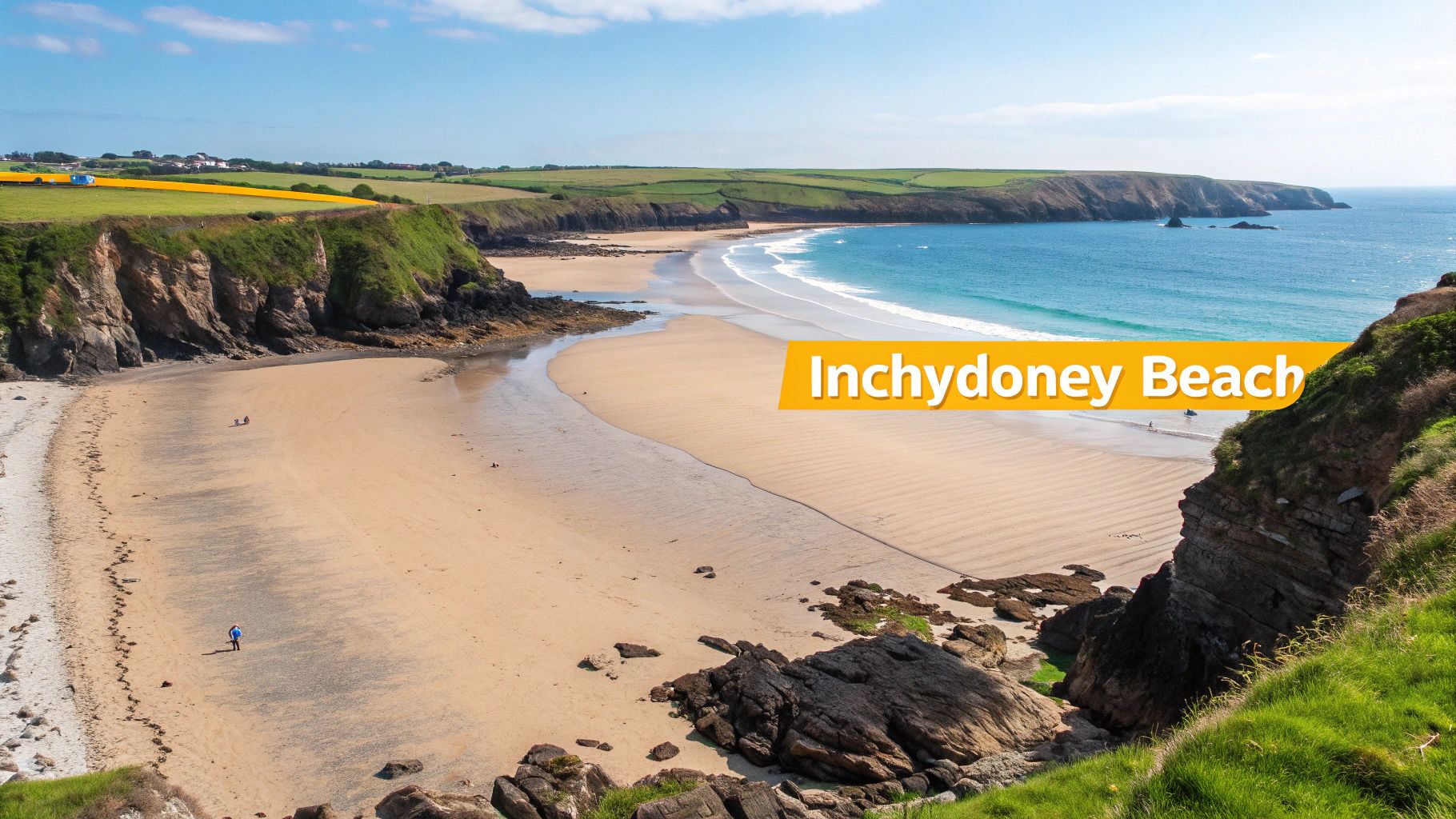 Scenic aerial view of Inchydoney Beach with golden sand, blue ocean, and green cliffs under a clear sky.