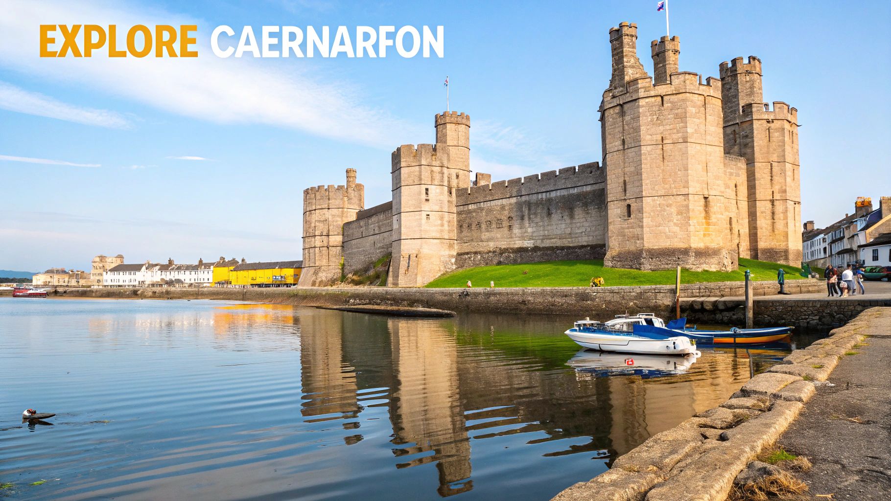 Panoramic view of Caernarfon Castle in Wales, reflecting on the tranquil waterfront with boats.