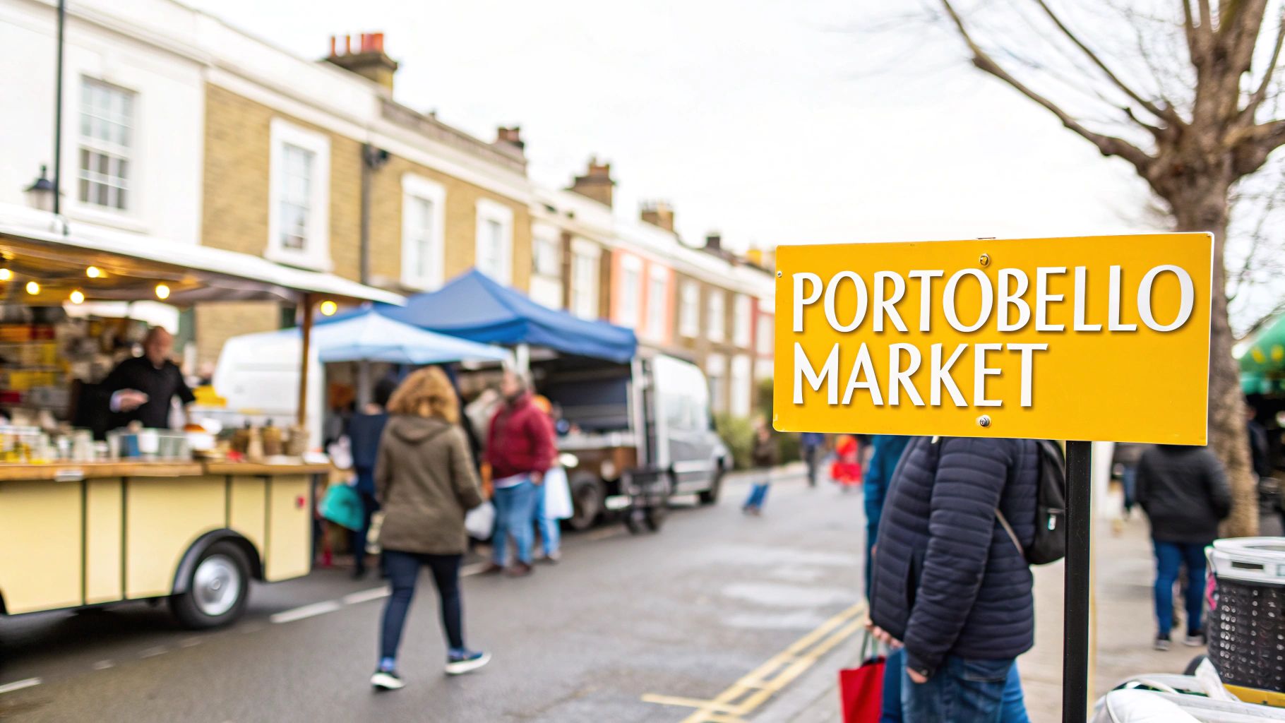 Visiting Notting Hill Your Ultimate Guide to London's Most Vibrant Neighbourhood 4 A bright yellow sign for Portobello Market stands prominently on a bustling street with various market stalls and shoppers.