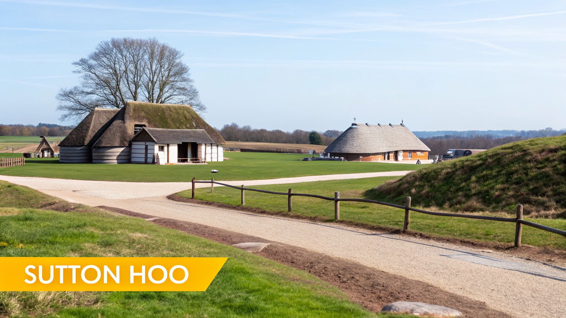 View of reconstructed Anglo-Saxon halls at Sutton Hoo, with a path and grassy mounds under a blue sky.
