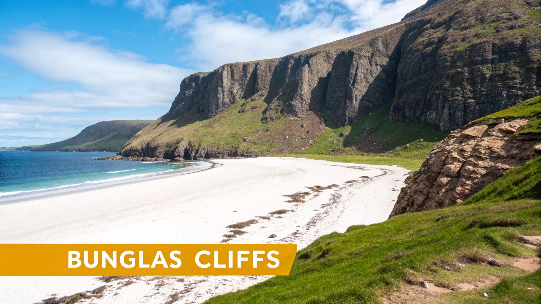 A picturesque white sand beach with turquoise water curves along dramatic green cliffs under a blue sky.