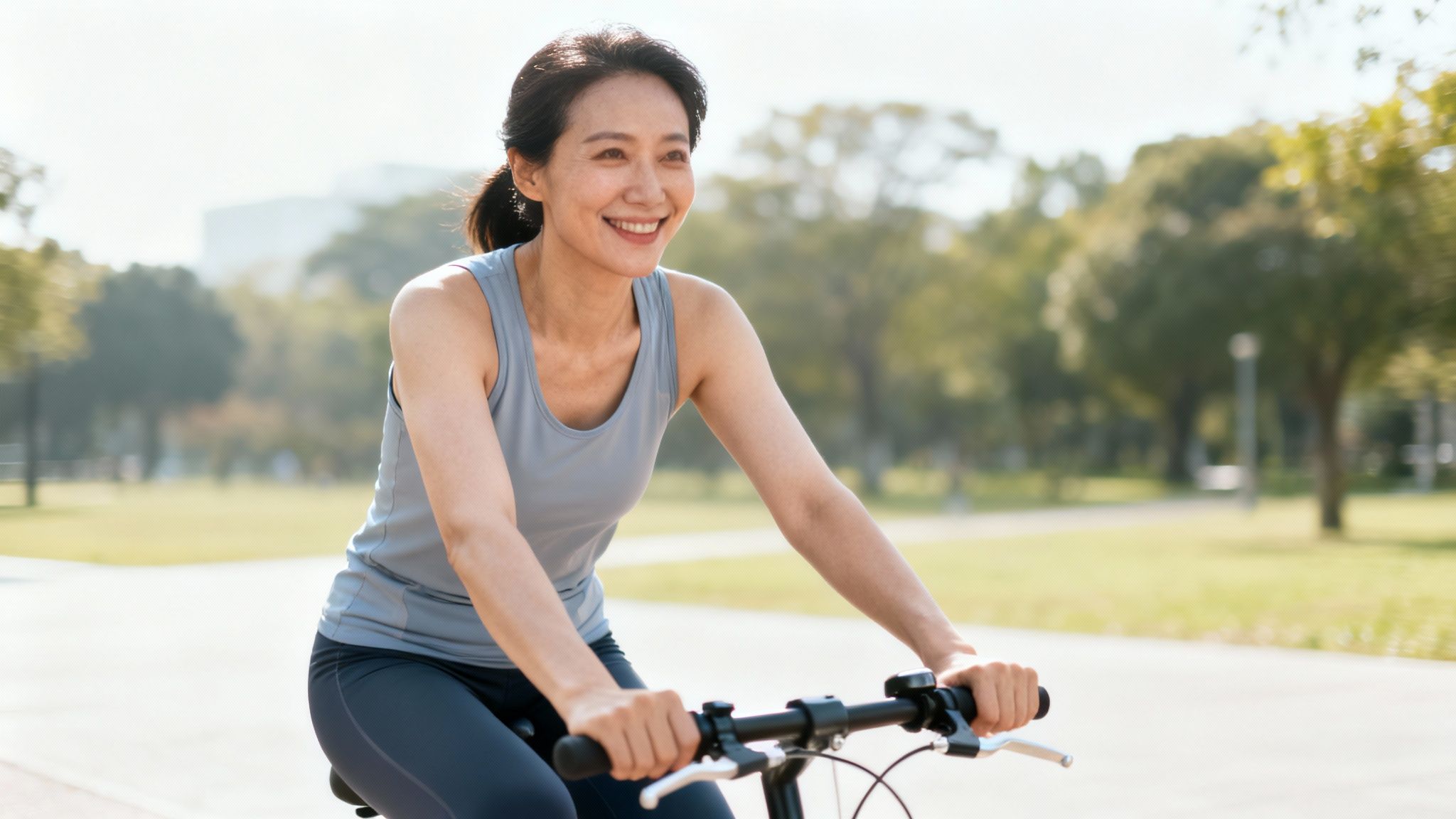 Mujer asiática sonriente y feliz andando en bicicleta por un parque verde y soleado.