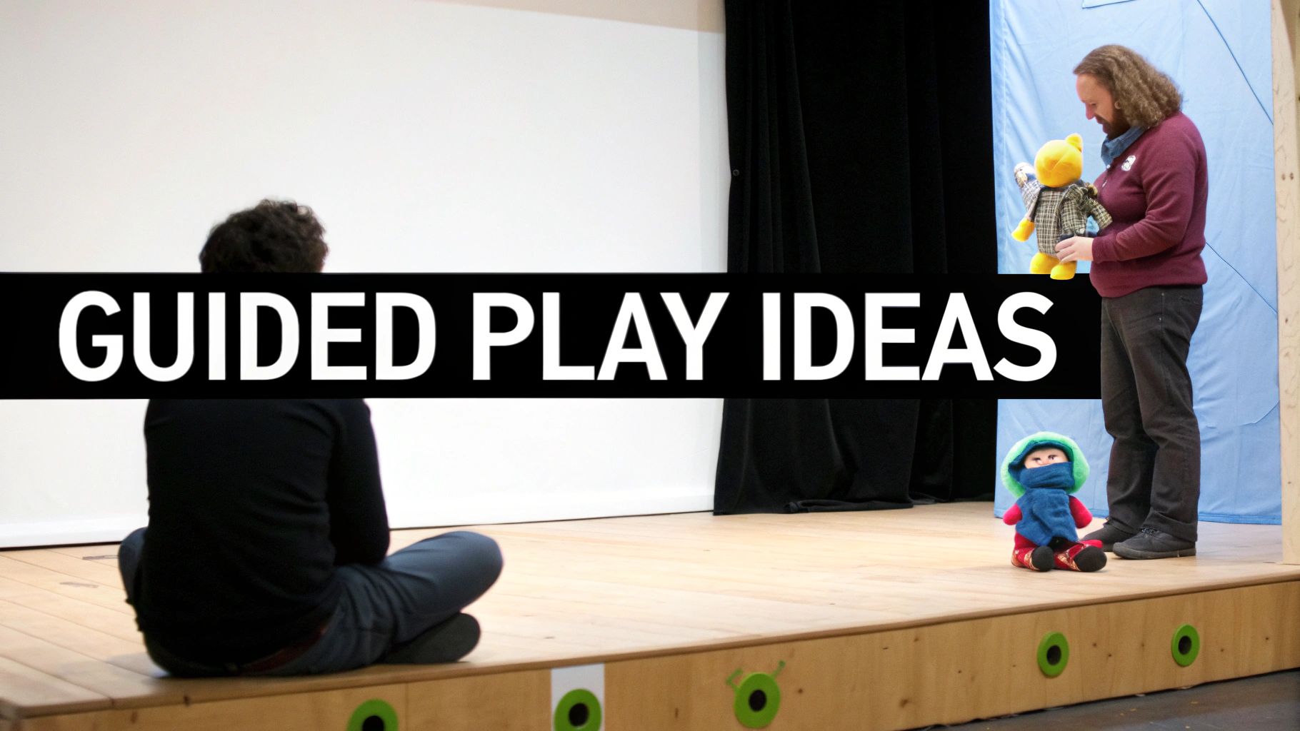 A man holds a teddy bear on a stage with another person sitting, displaying 'GUIDED PLAY IDEAS' text.