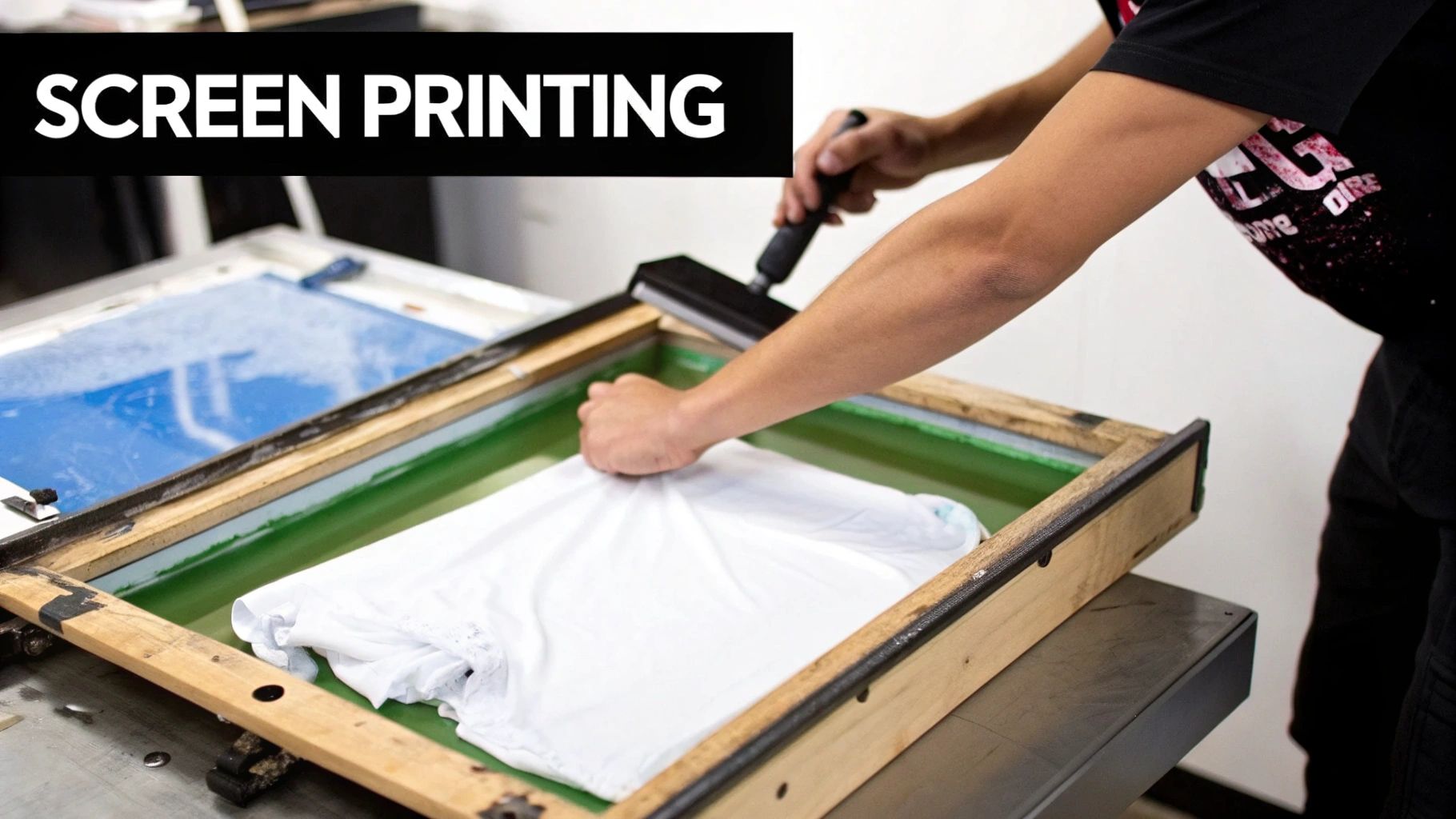 A person actively screen printing a white t-shirt with green ink using a squeegee and a frame.