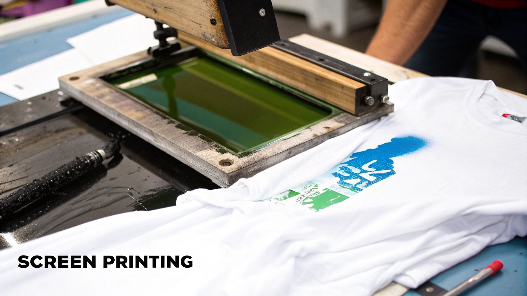 A screen printing press in action, showing a squeegee pushing ink across a mesh screen onto a t-shirt.
