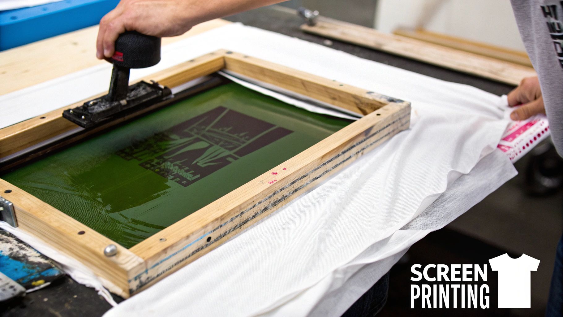 A squeegee pushing ink across a mesh screen to print a design on a t-shirt