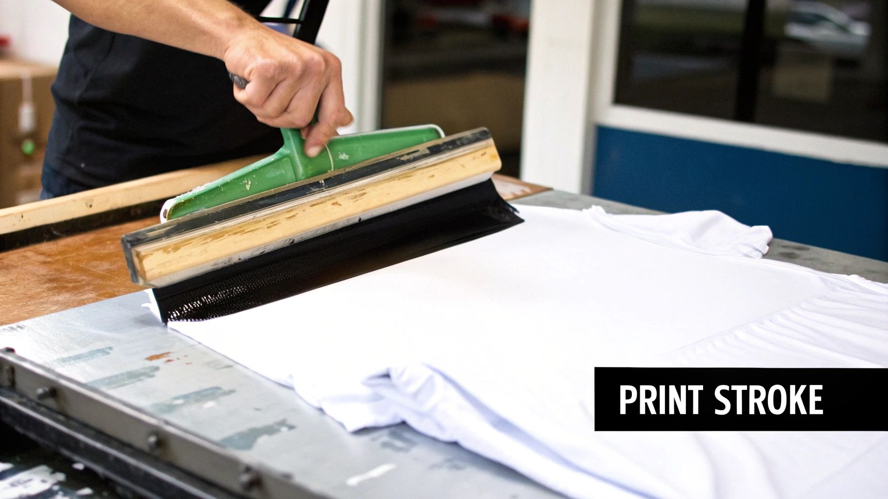 A screen printer pulling ink across a screen to print on a t-shirt.