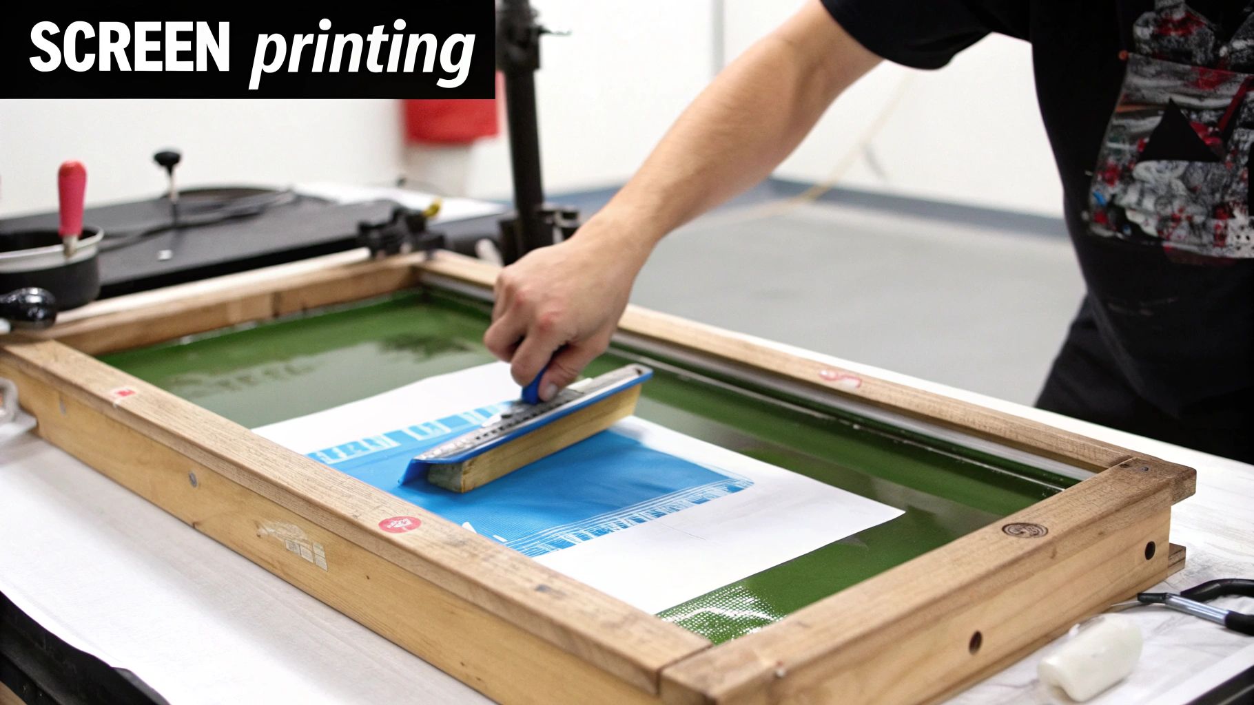 A person screen printing a design onto a blue sheet using a squeegee and a wooden frame.