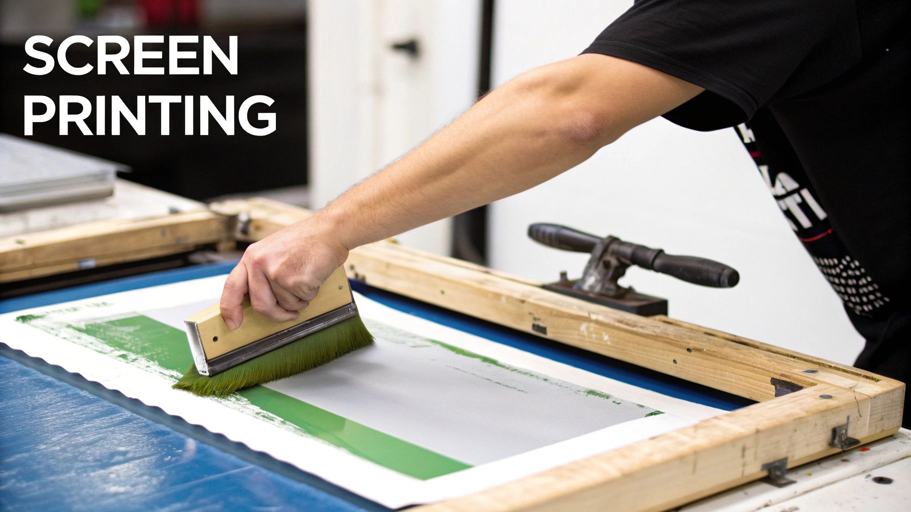 A person uses a squeegee to apply green ink during the screen printing process.
