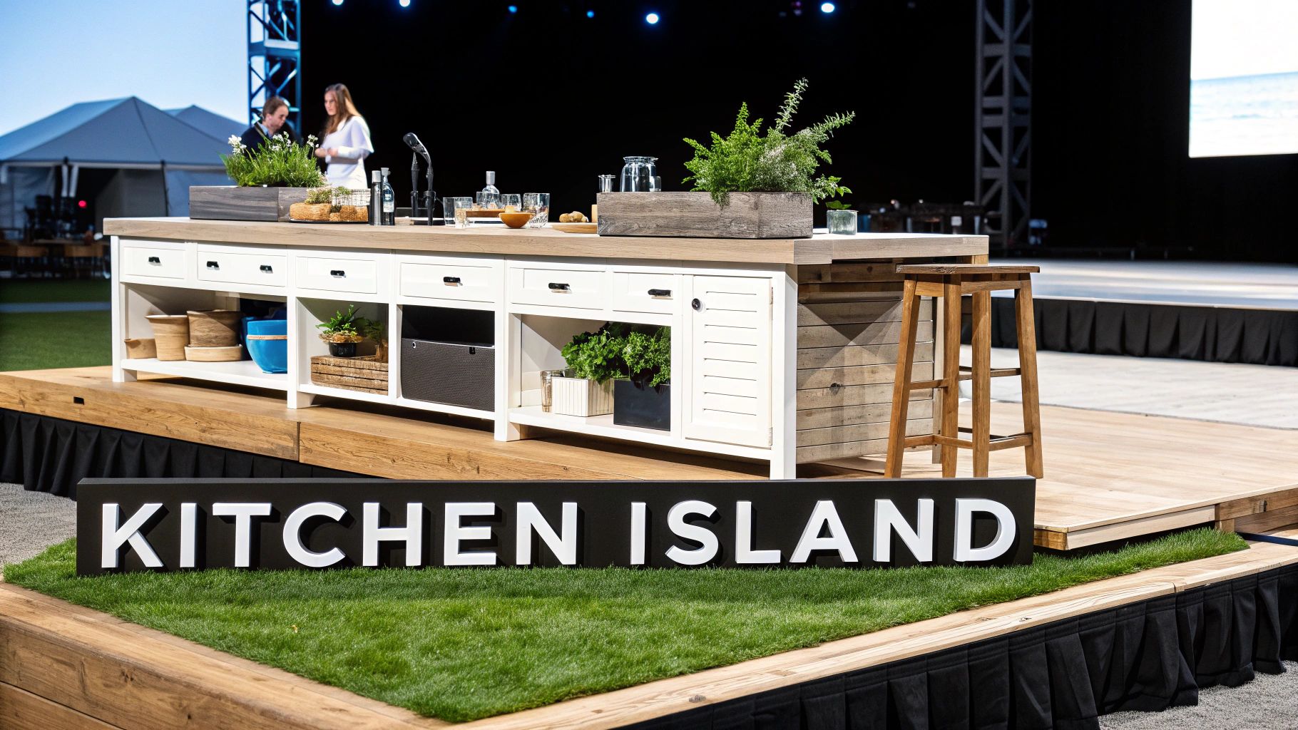 A stylish kitchen island with plants, cooking items, and a wooden stool on a stage.