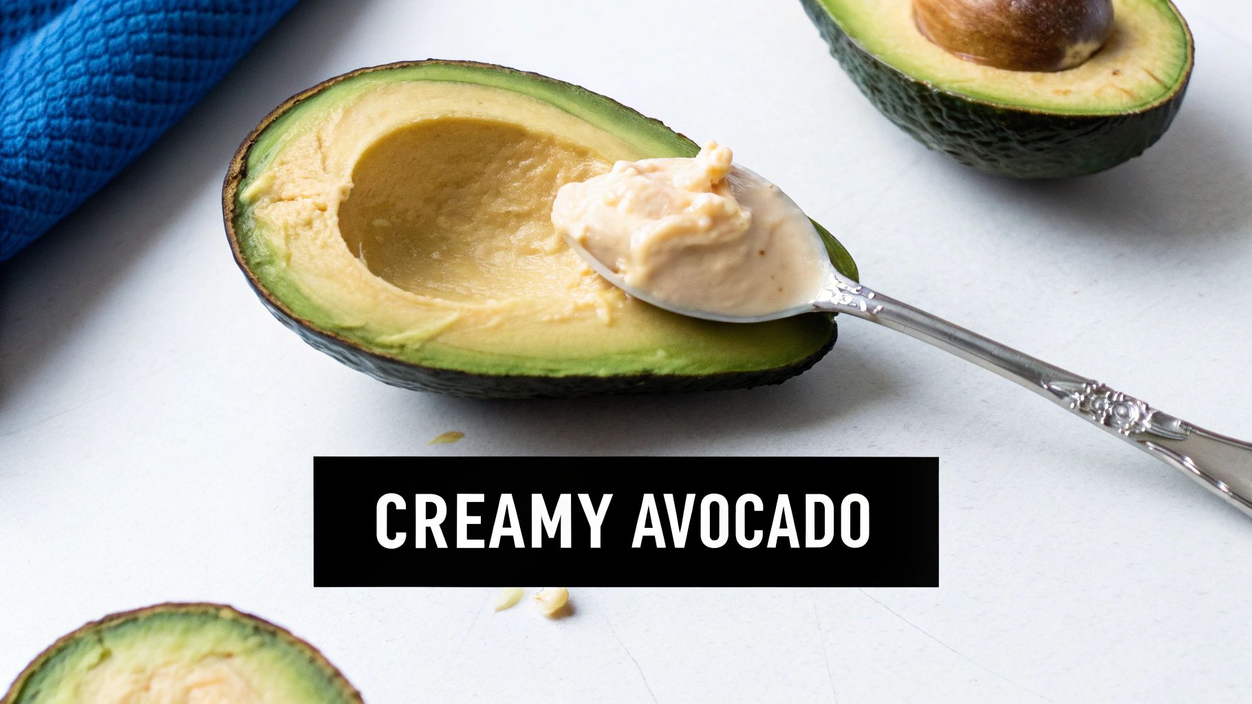 A close-up of a halved avocado with a spoonful of creamy filling, on a white surface.