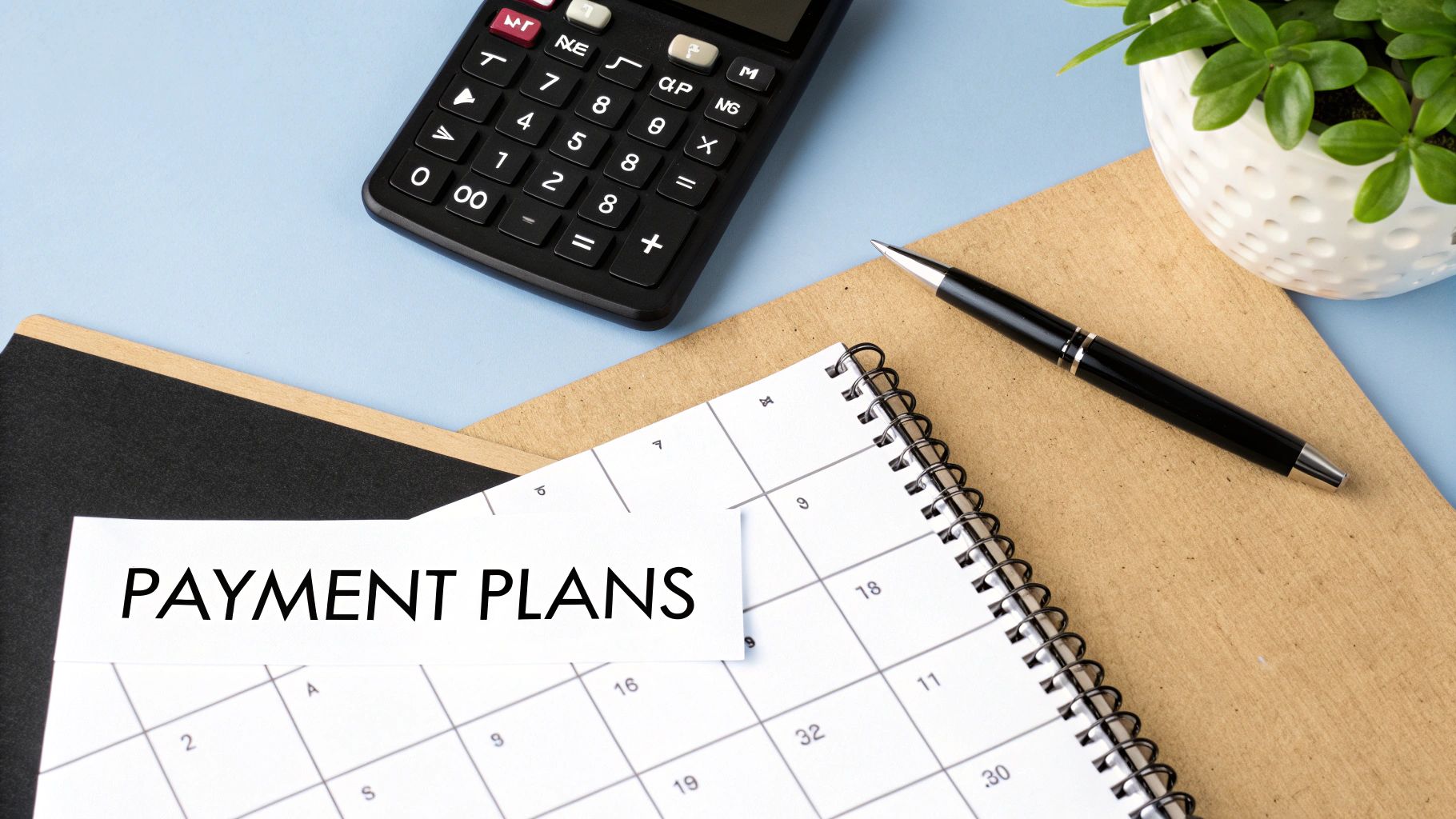 A flat lay of a calculator, pen, calendar with 'PAYMENT PLANS' text, and a plant on a blue desk.