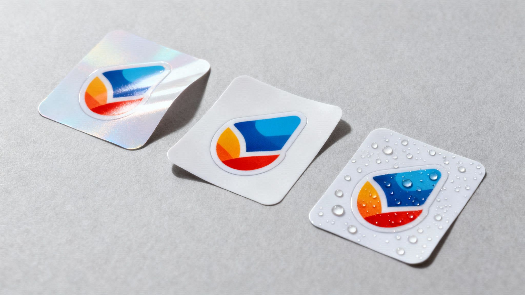 Three custom stickers on a grey background: holographic, matte white, and water-resistant with droplets.
