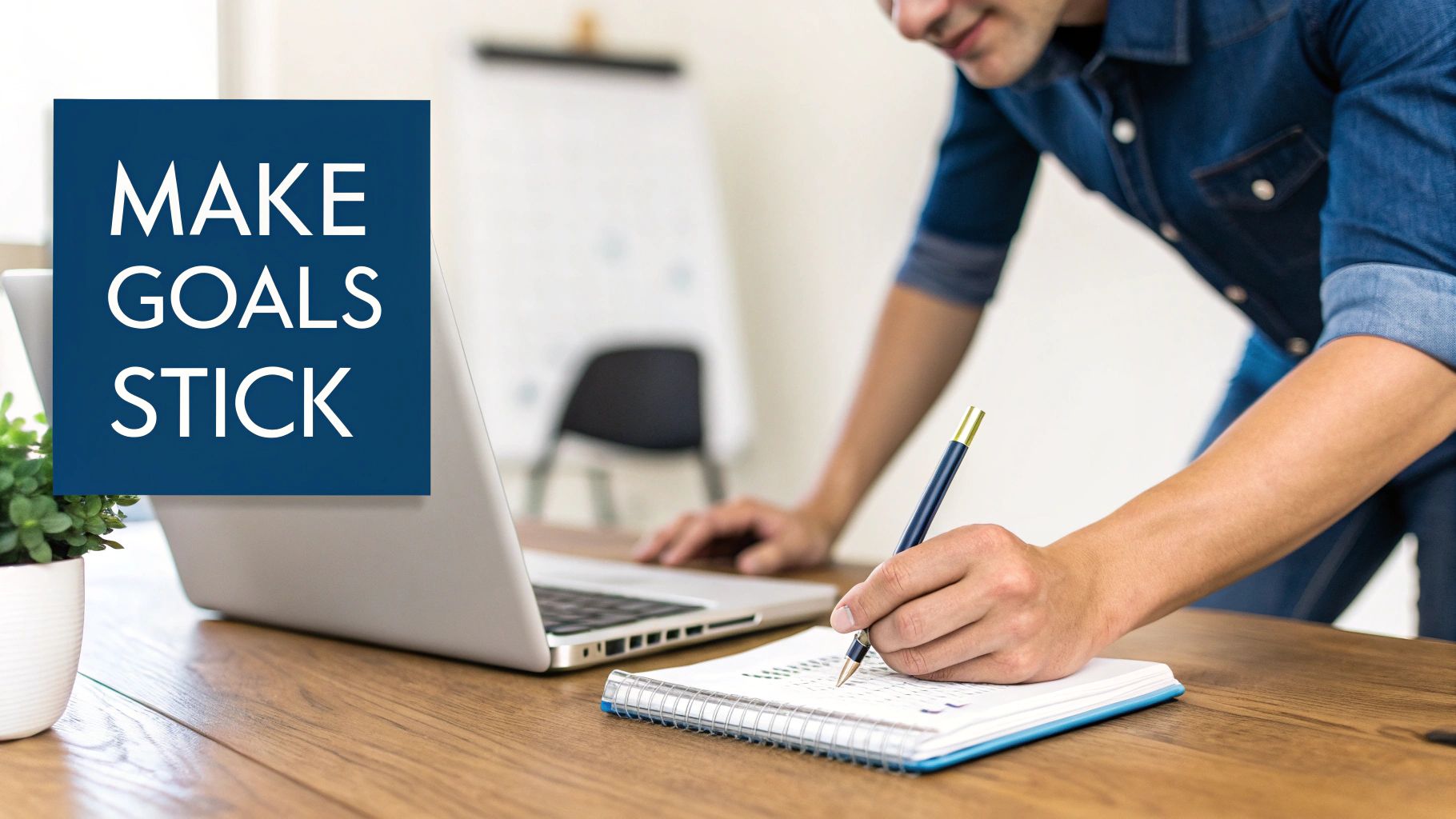 A person writing in a notebook next to a laptop on a wooden desk, planning goals.
