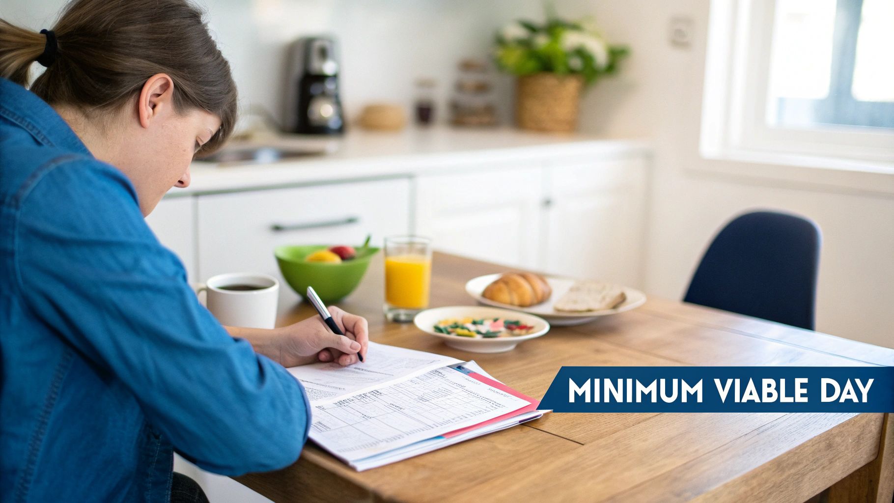 Person in blue shirt writing at a kitchen table surrounded by breakfast food and coffee.