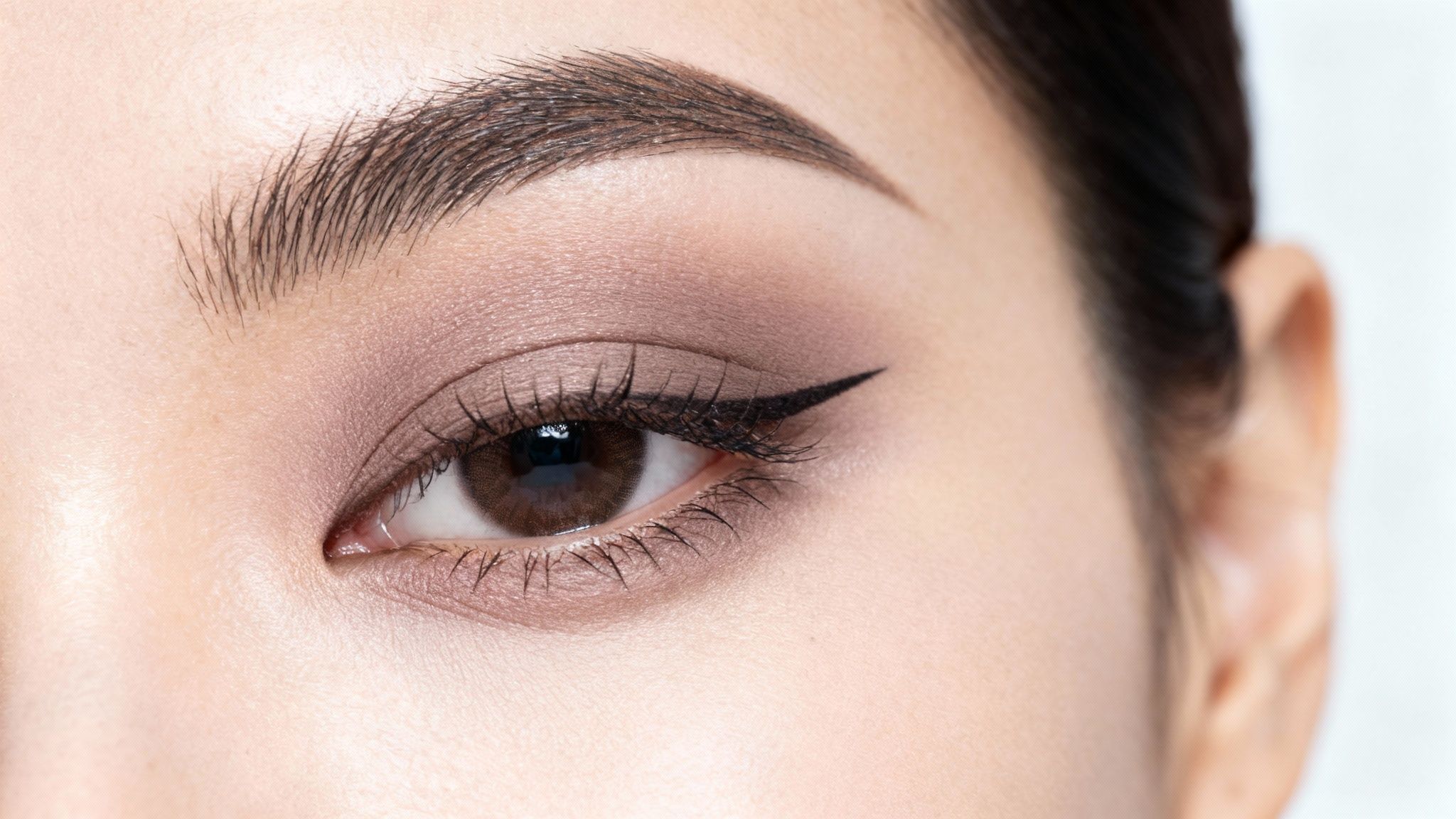 Zbliżenie oka kobiety z makijażem, brązowym cieniem i wyrazistą kreską eyelinera.
