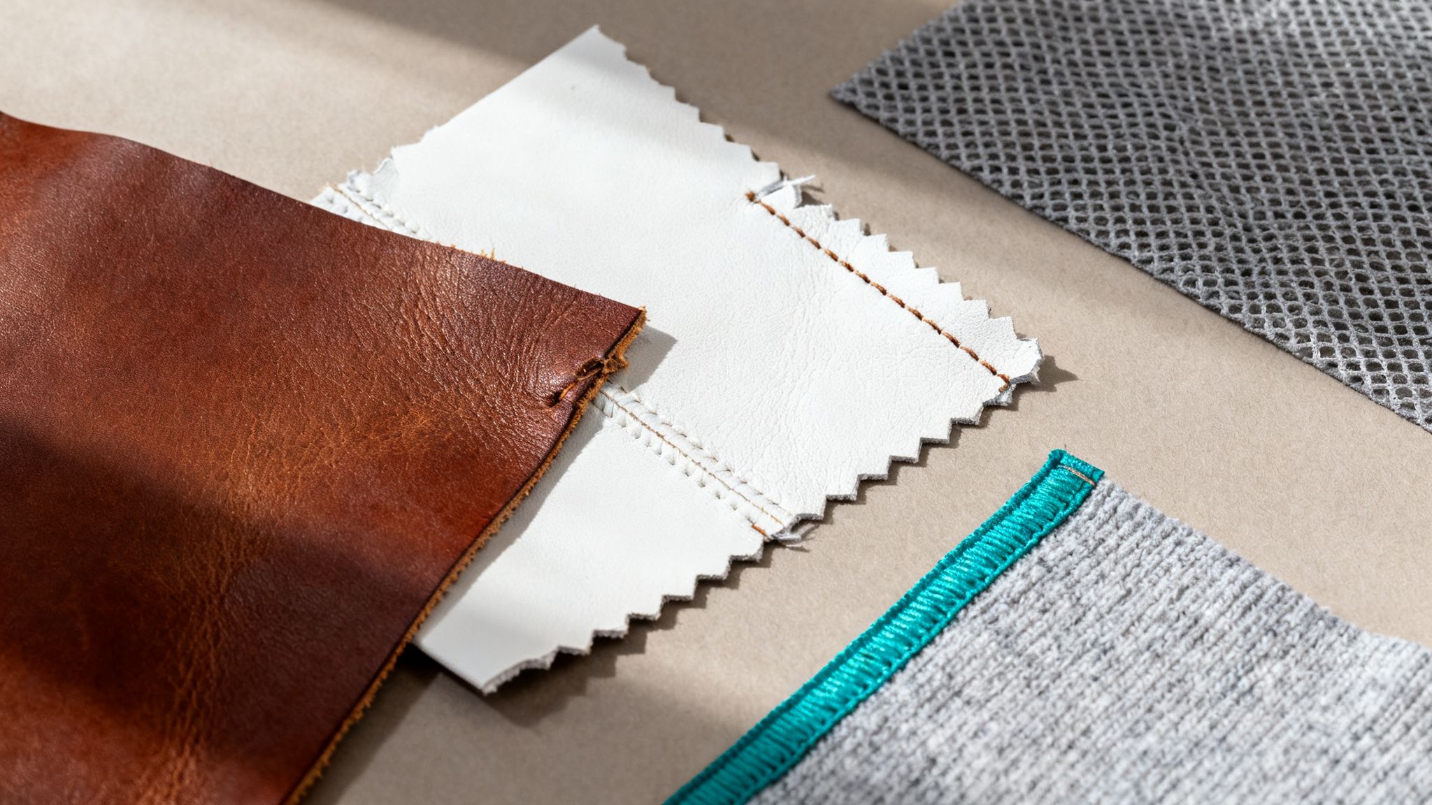 Próbki materiałów: brązowa skóra, biała ekoskóra, szara siatka, dzianina z turkusowym obszyciem na beżowym tle.