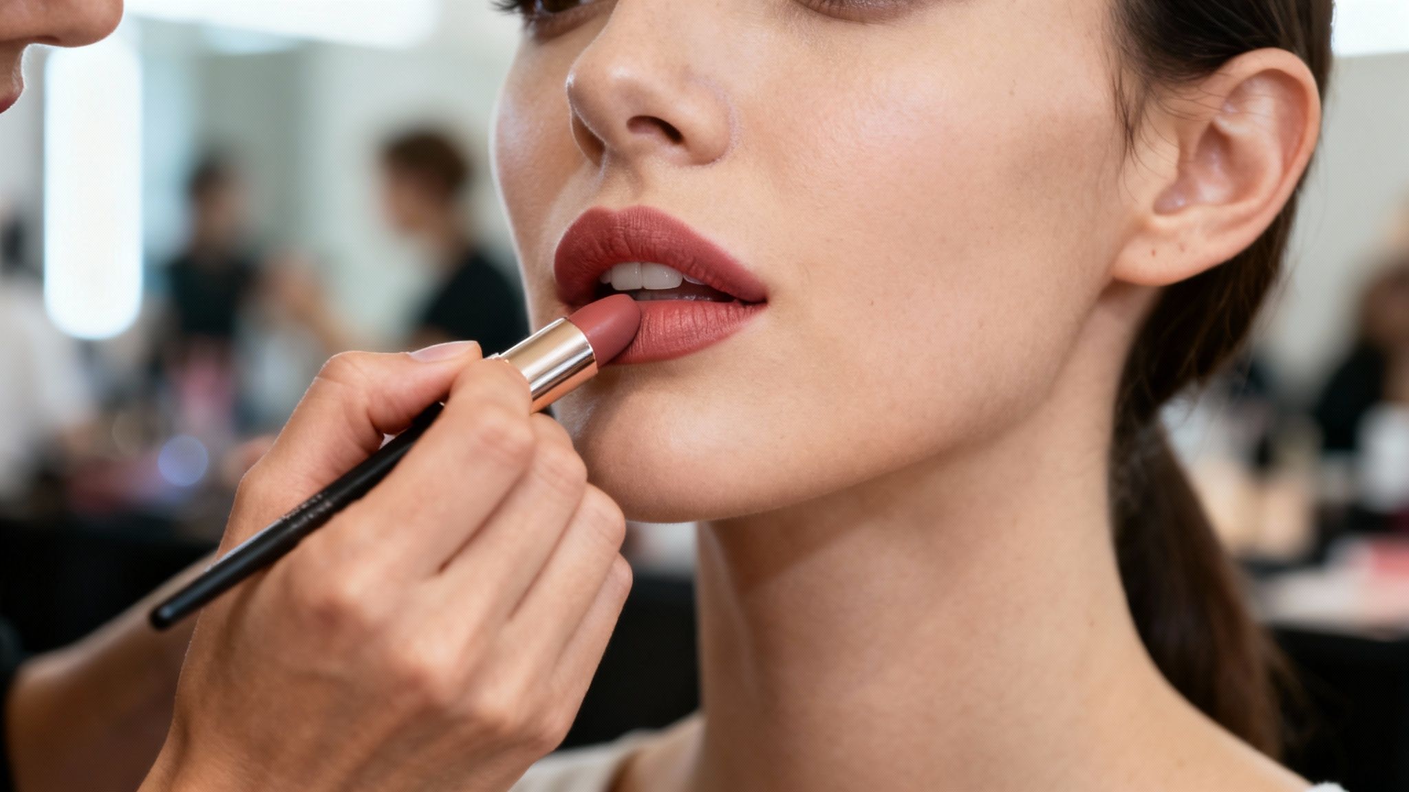 Ręka wizażysty nakładająca szminkę pędzelkiem na usta modelki w zbliżeniu.