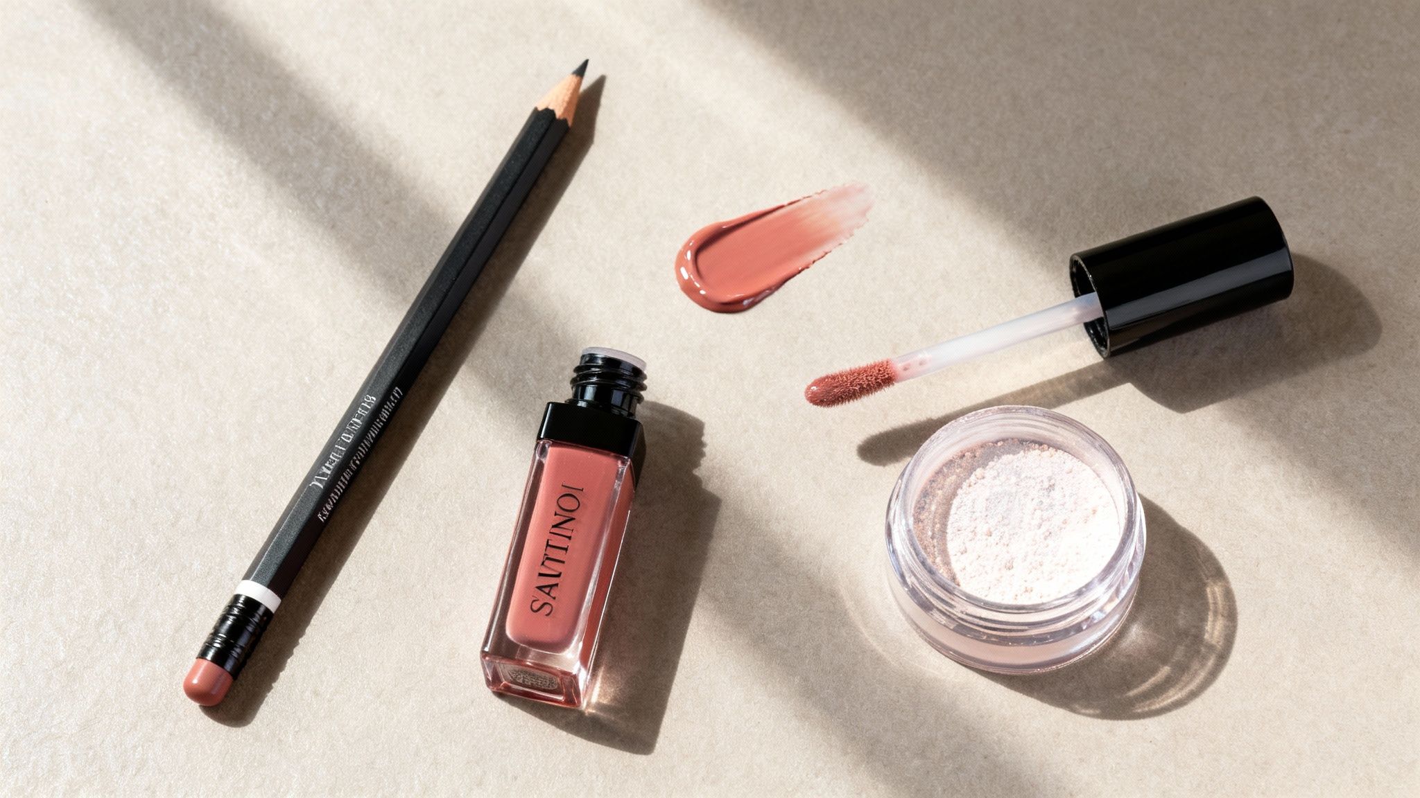 Makijażowe produkty w odcieniach nude: kredka do ust, błyszczyk z aplikatorem i sypki puder na stole.