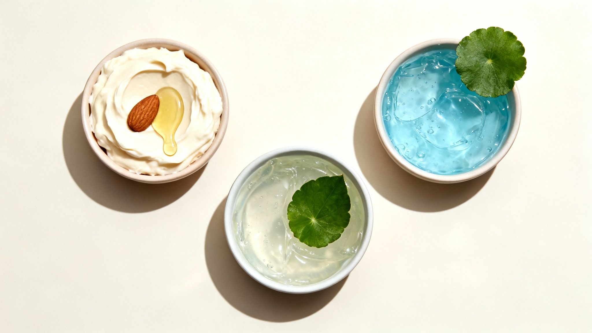 Trzy miseczki z kremami i żelami do pielęgnacji skóry, ozdobione migdałem, miodem i zielonymi liśćmi.