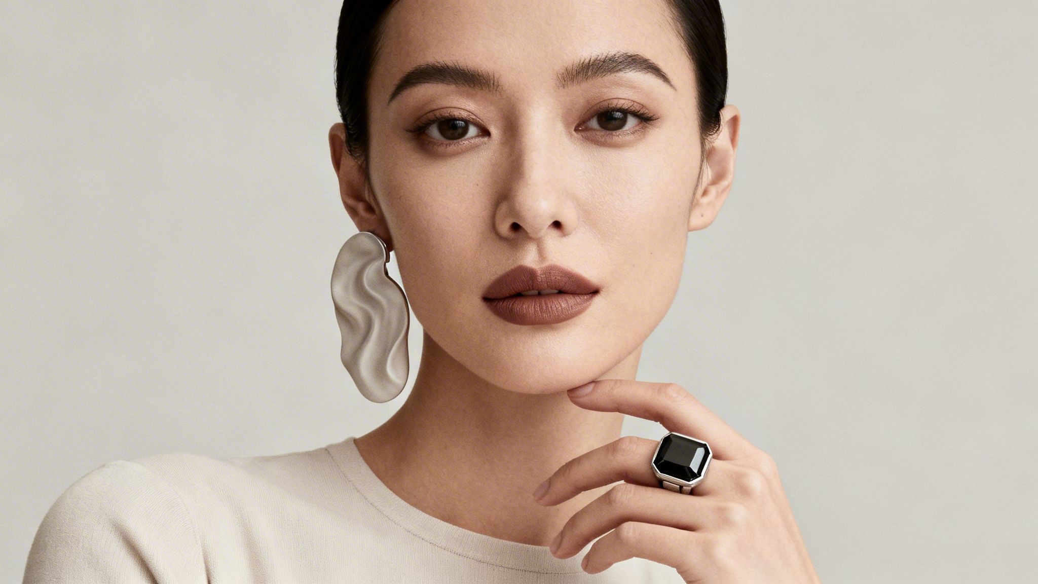 Kobieta z ciemnymi włosami w dużych, srebrnych kolczykach i pierścionku z czarnym kamieniem.